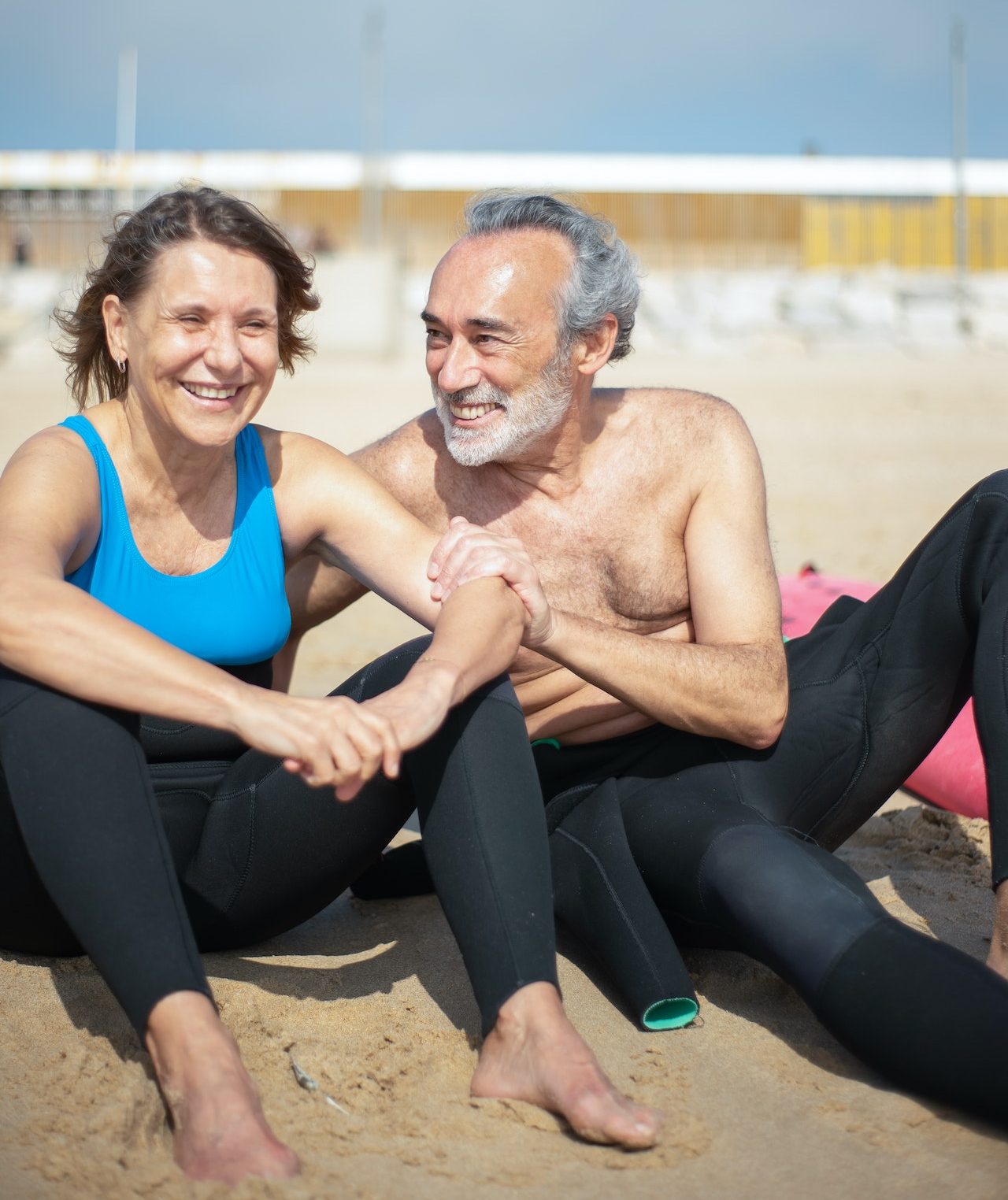 senior man and woman on sunny beach in wetsuits