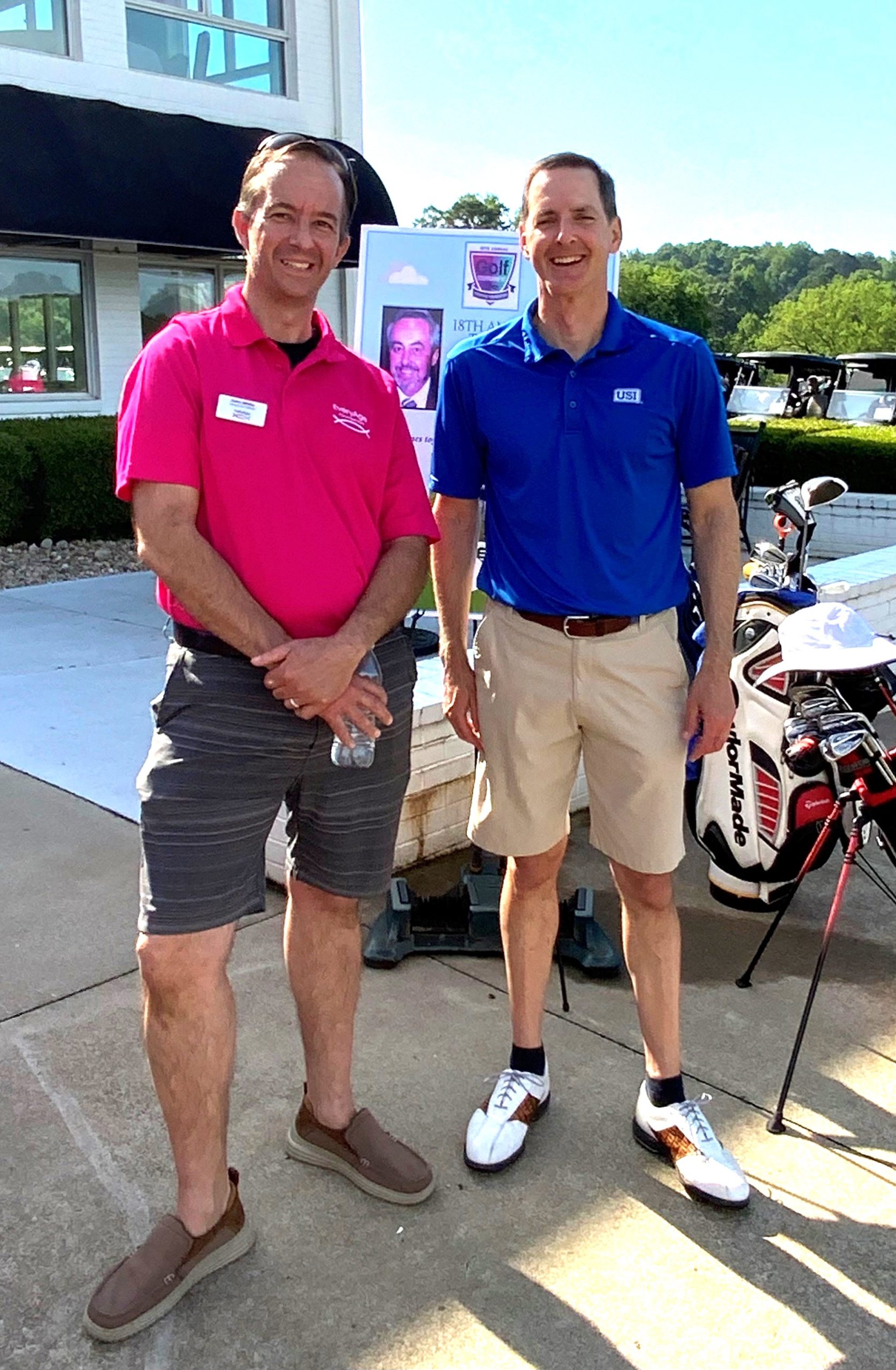 Two men standing at golf tournament, wearing polo shirts and shorts