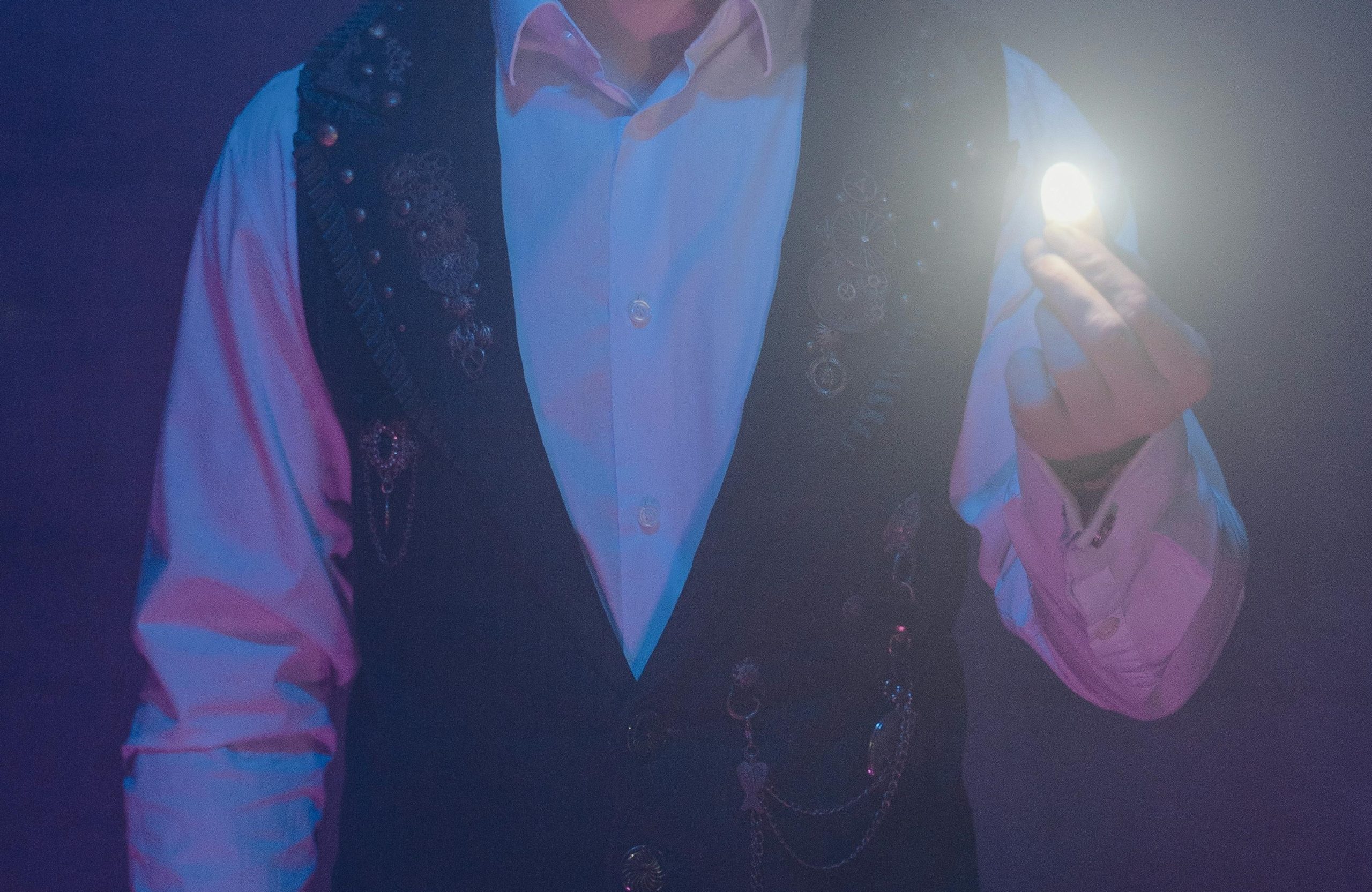 torso of man in white shirt and black vest holding light in his fingers